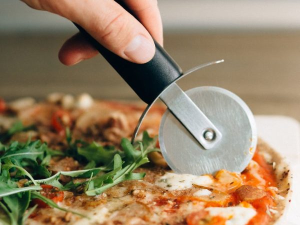person holding black handled knife slicing pizza