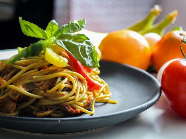 pasta with vegetable dish on gray plate beside tomato fruit on white table